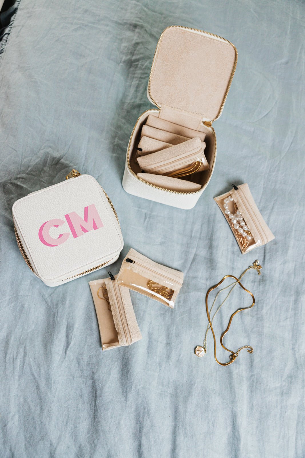 A stylish and functional personalized jewelry travel case set in white, featuring a compact square design with initials "KS" in blue on the exterior. One case is closed, showcasing its sleek and durable outer shell, while the other is open, revealing a soft beige interior with multiple compartments and zippered pouches for secure and organized storage of rings, earrings, necklaces, and other accessories. This elegant set is perfect for keeping jewelry safe and tangle-free while traveling.